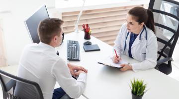 A woman doctor sits at a desk with a patient discussing his care