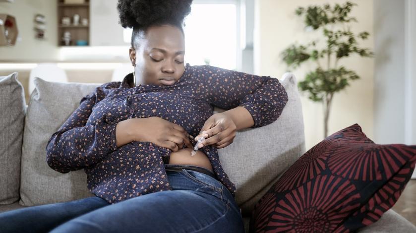 A black woman gives herself an injection of a weight loss drug.