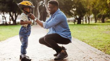 A father checks his young son's bike helmet before he goes for a bike ride.