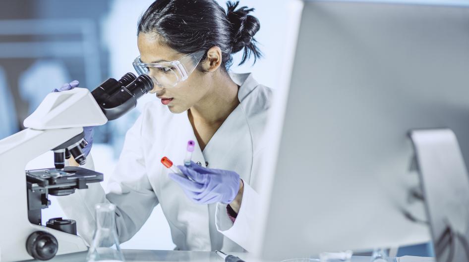 A young woman doctor looks into a microscope while conducting clinical research