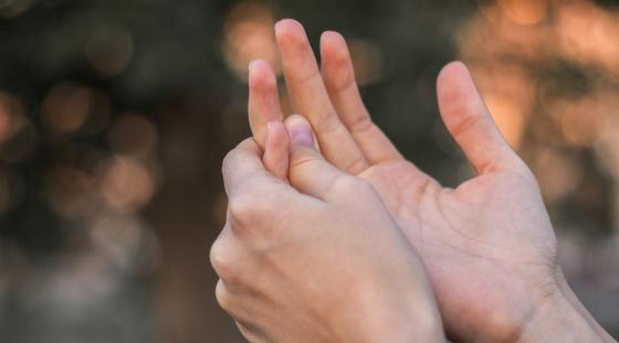A close up view of two hands as a person holds one of their fingers due to finger pain.