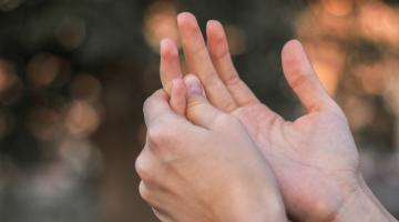 A close up view of two hands as a person holds one of their fingers due to finger pain.