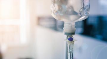 A close up view of an IV fluid bag with a home view in the background
