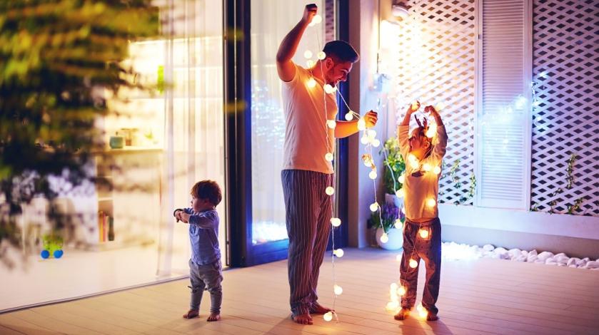A dad with his two young children getting ready to hang holiday lights