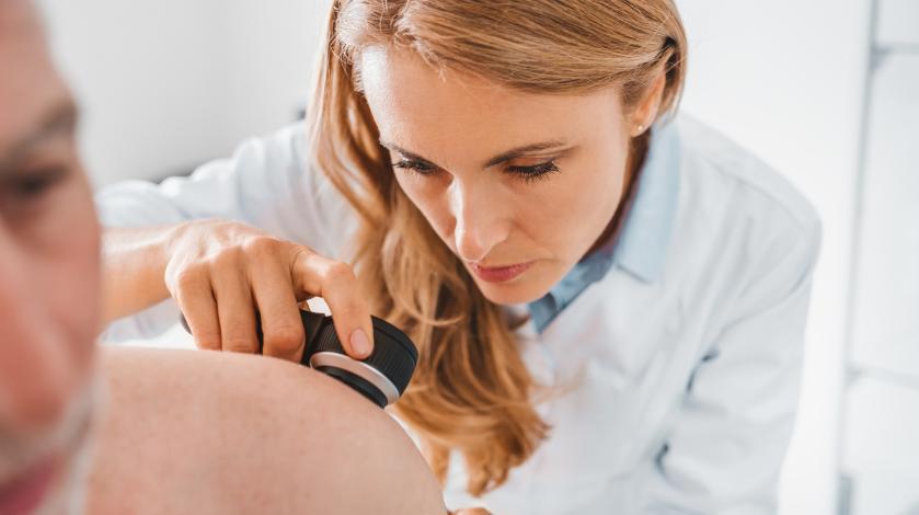 A female dermatologist screens a male patient for skin cancer