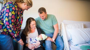 New mother and father holding child with nurse