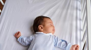 A baby sleeps on his back in an empty crib safe sleep