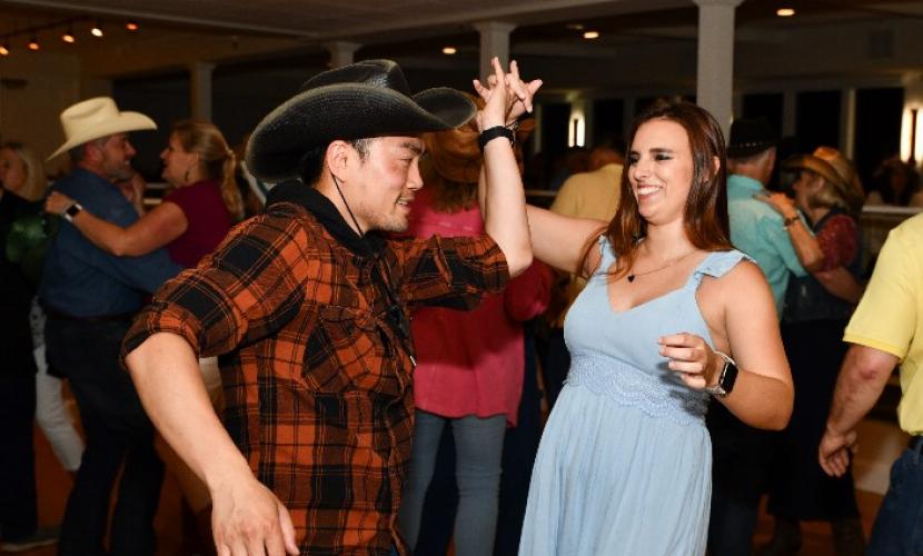 A man in a cowboy hat and plaid shirt dances with a woman at South Shore Health's 2022 Kickin' Up Country event.
