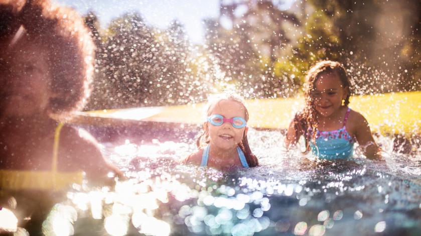 A group of kids splashes and laughs while swimming in a pool