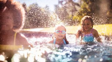 A group of kids splashes and laughs while swimming in a pool