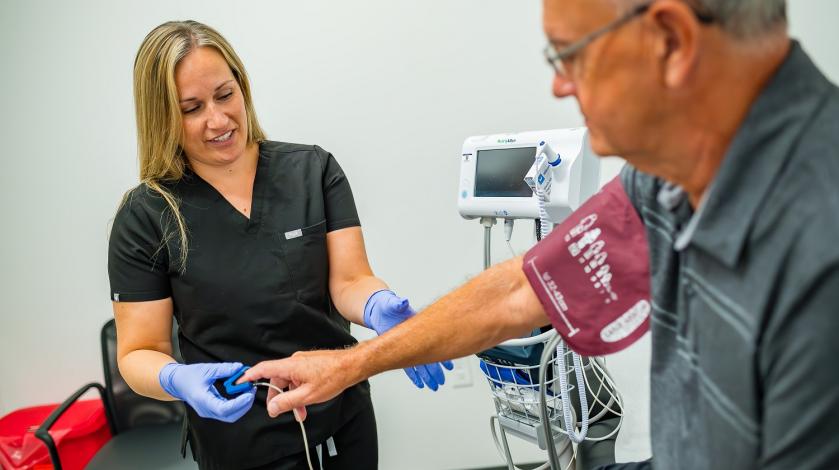 An urgent care clinician checks the pulse and blood pressure of an older male patient