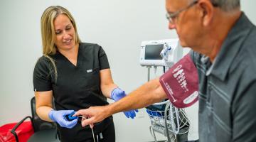 An urgent care clinician checks the pulse and blood pressure of an older male patient