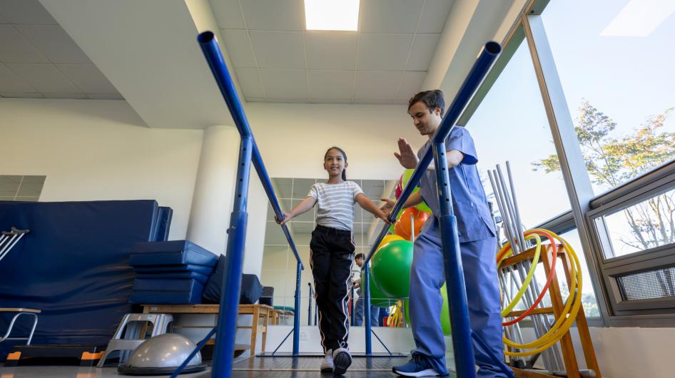 A pediatric physical therapy patient walking with balance bars