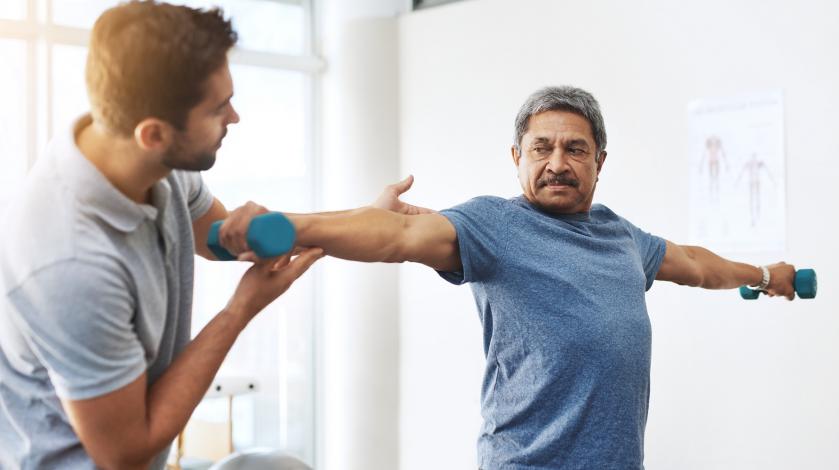 A patient holding a weight while working with a physical therapist