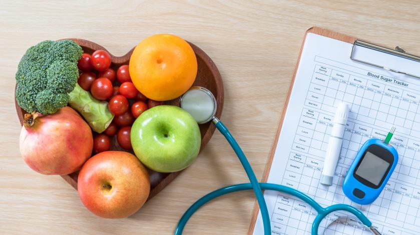 Heart shaped bowl of fruit with diabetes monitor and meal plan