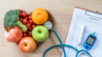 Heart shaped bowl of fruit with diabetes monitor and meal plan