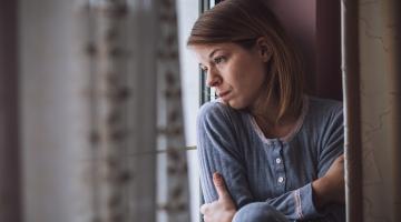 A woman looks out the window sadly on a day that seems kind of gray and dull.