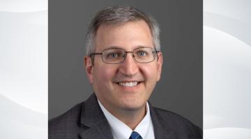 Professional headshot of Sam Skura, COO of South Shore Health, on a gray wave patterned background
