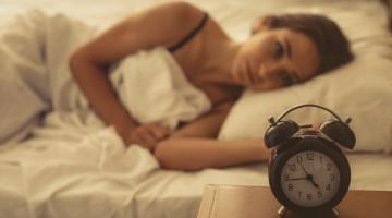 A woman lies in bed unable to sleep and watching the clock