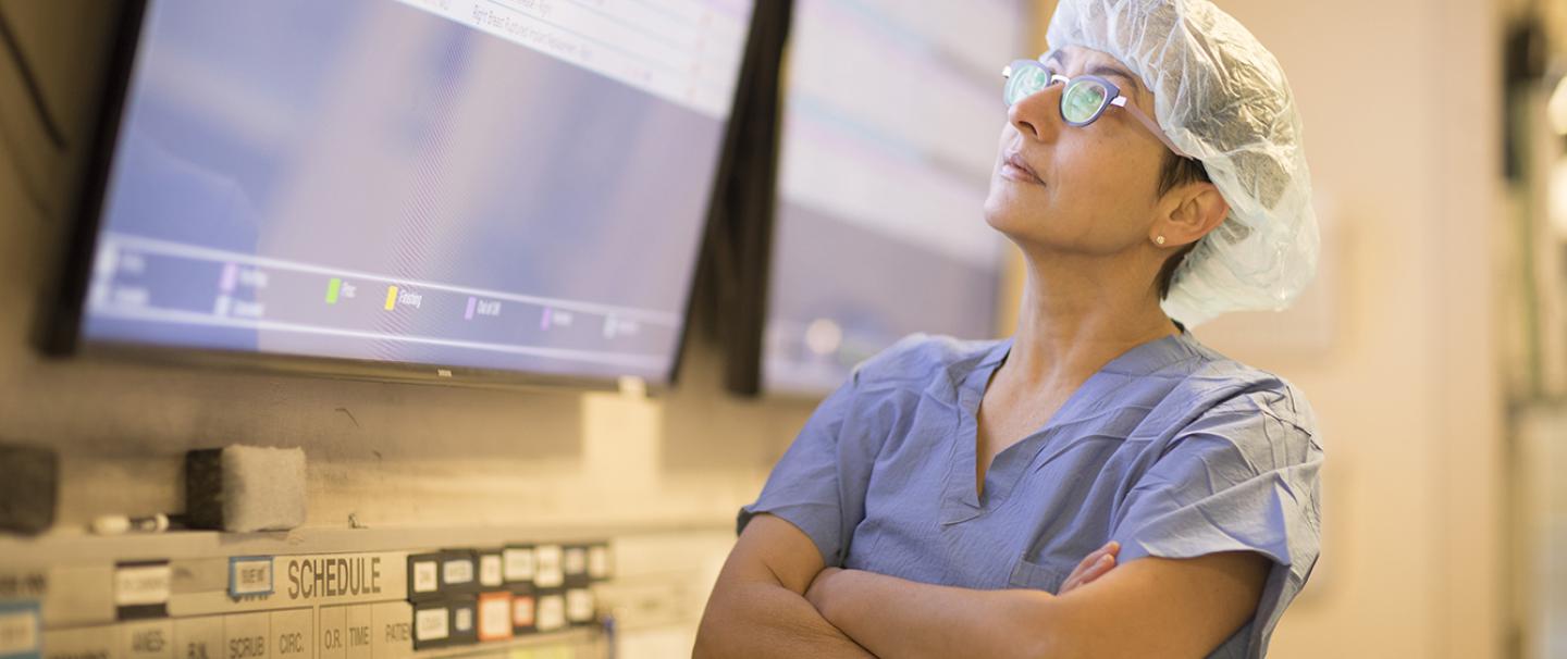 Doctor wearing scrubs looks up at screen