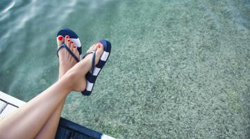 A woman wearing flip flops hangs her legs over the edge of a pier