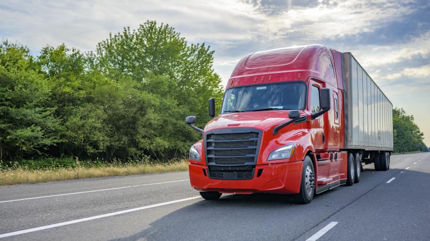 A red semi truck hauling a trailer drives down the road in the sunshine