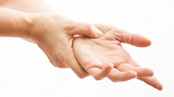 Close-up view of a woman's hands as she uses her right hand to apply acupressure to her left palm