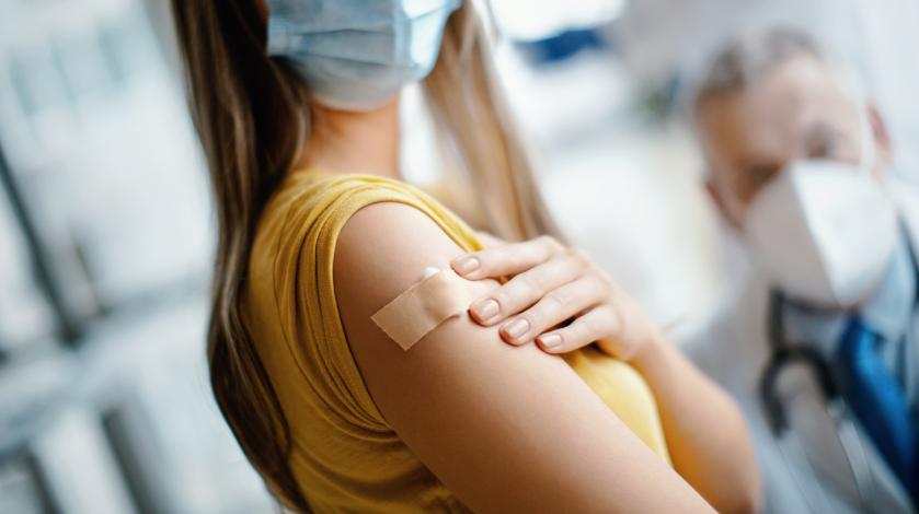 A woman wearing a mask shows the band aid on her arm after getting a COVID-19 vaccine