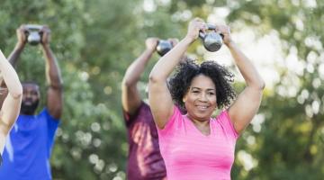 A Black woman works out with weights in a group outdoors