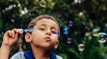 A young boy blows bubbles with a bubble wand while playing outside