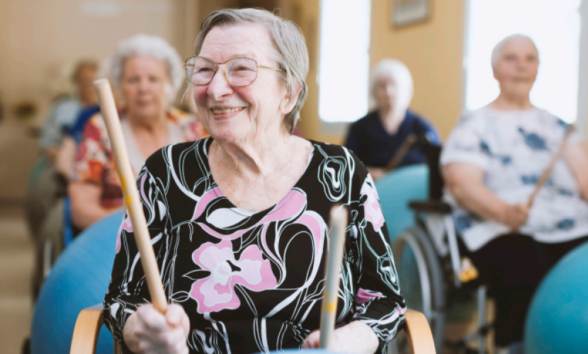 An older woman smiles as she holds drumsticks as part of therapy in a stroke support group